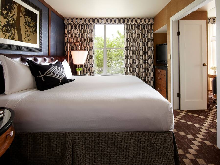 A hotel room with a large bed, a TV, a desk with a lamp, and a view of the outdoors.