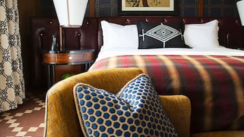 A hotel room with a bed, a nightstand, a lamp, a chair, and a patterned throw blanket.