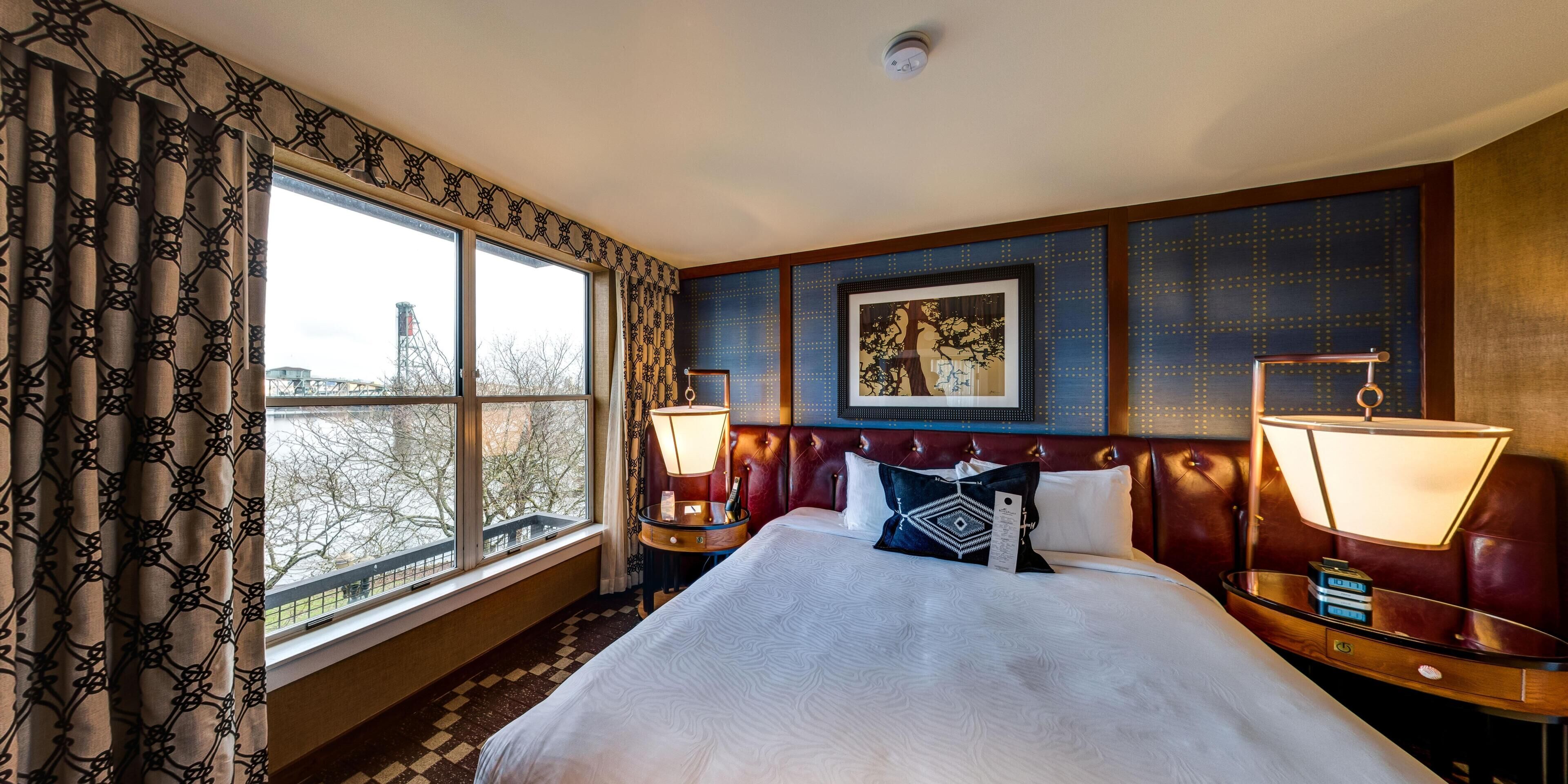 Une chambre d’hôtel avec un grand lit, deux lampes de chevet, une œuvre d’art encadrée au mur et une fenêtre avec des rideaux.