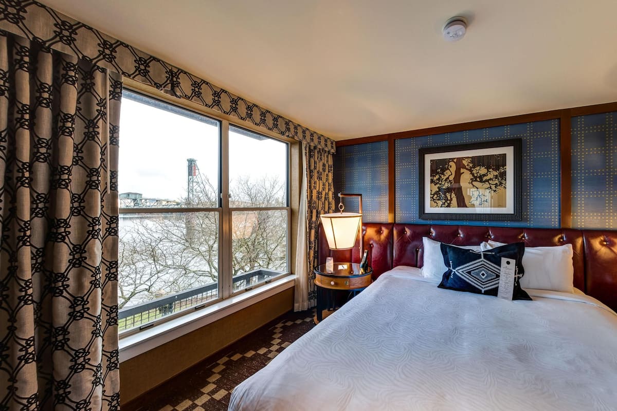 A hotel room with a large bed, two bedside lamps, a framed artwork on the wall, and a window with curtains.