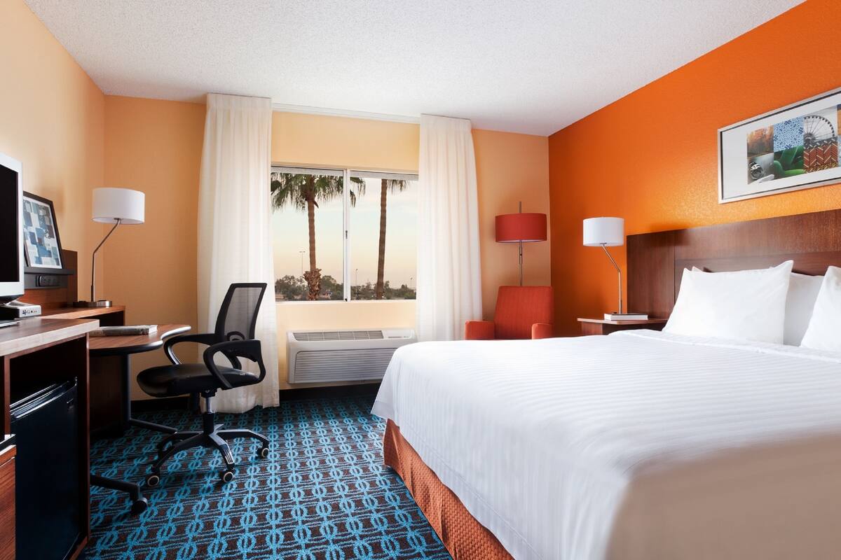 A hotel room with a bed, desk, chair, and a window with curtains.
