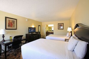 A hotel room with two beds, a desk, a television, and a mirror. - Plaza Inn (Midland)