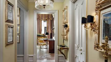 A hallway with a chandelier, framed artwork, and a mirror with ornate gold detailing.