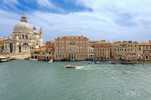 Un edificio storico con una grande cupola e strutture adiacenti più piccole, un canale con barche e cielo sereno.