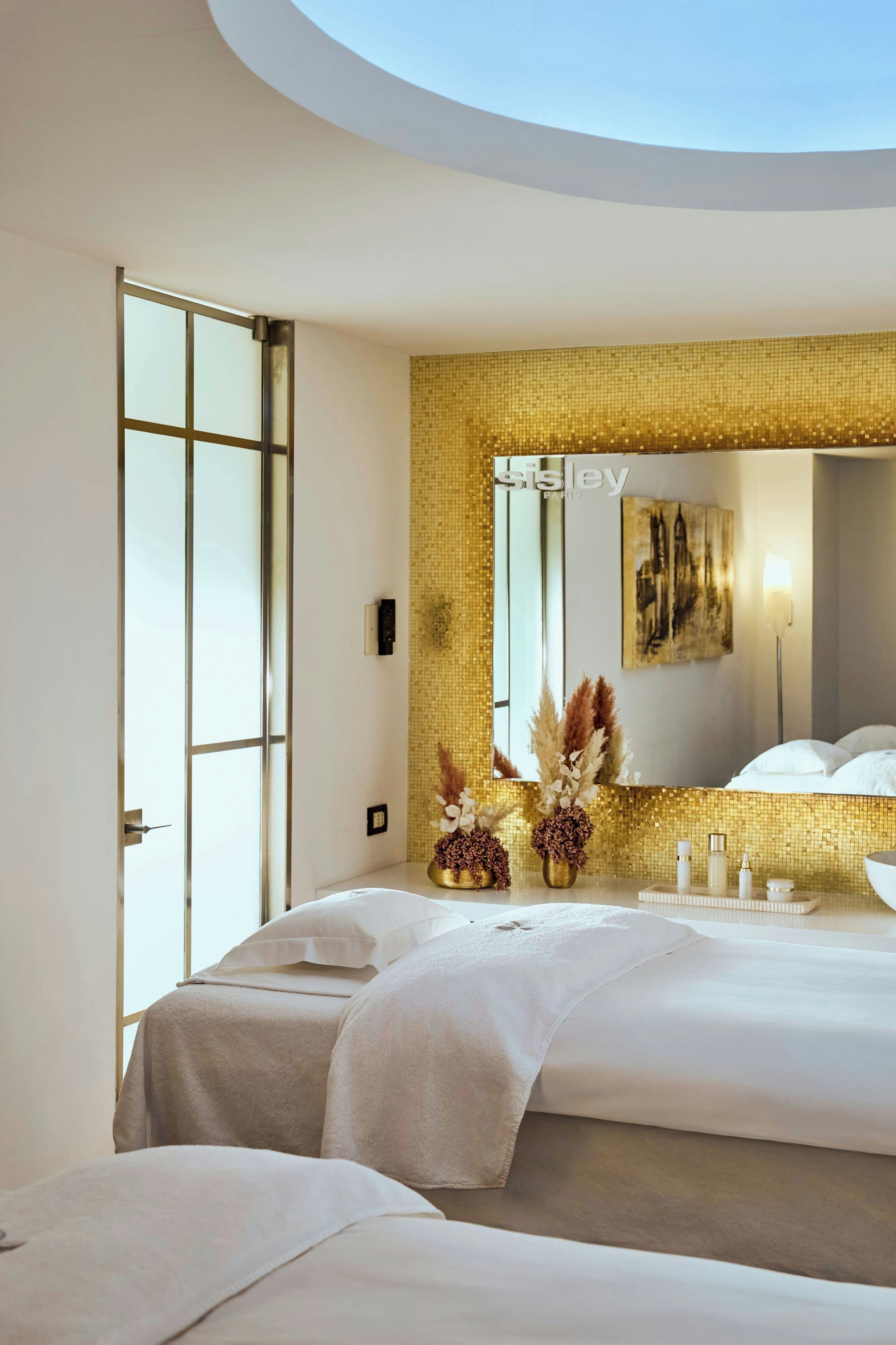 Una camera d'albergo moderna con un letto grande, un bagno con una parete in mosaico dorato e un lucernario.