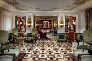 A grand lobby with a checkered floor, ornate chairs, and a central seating area with a red sofa.