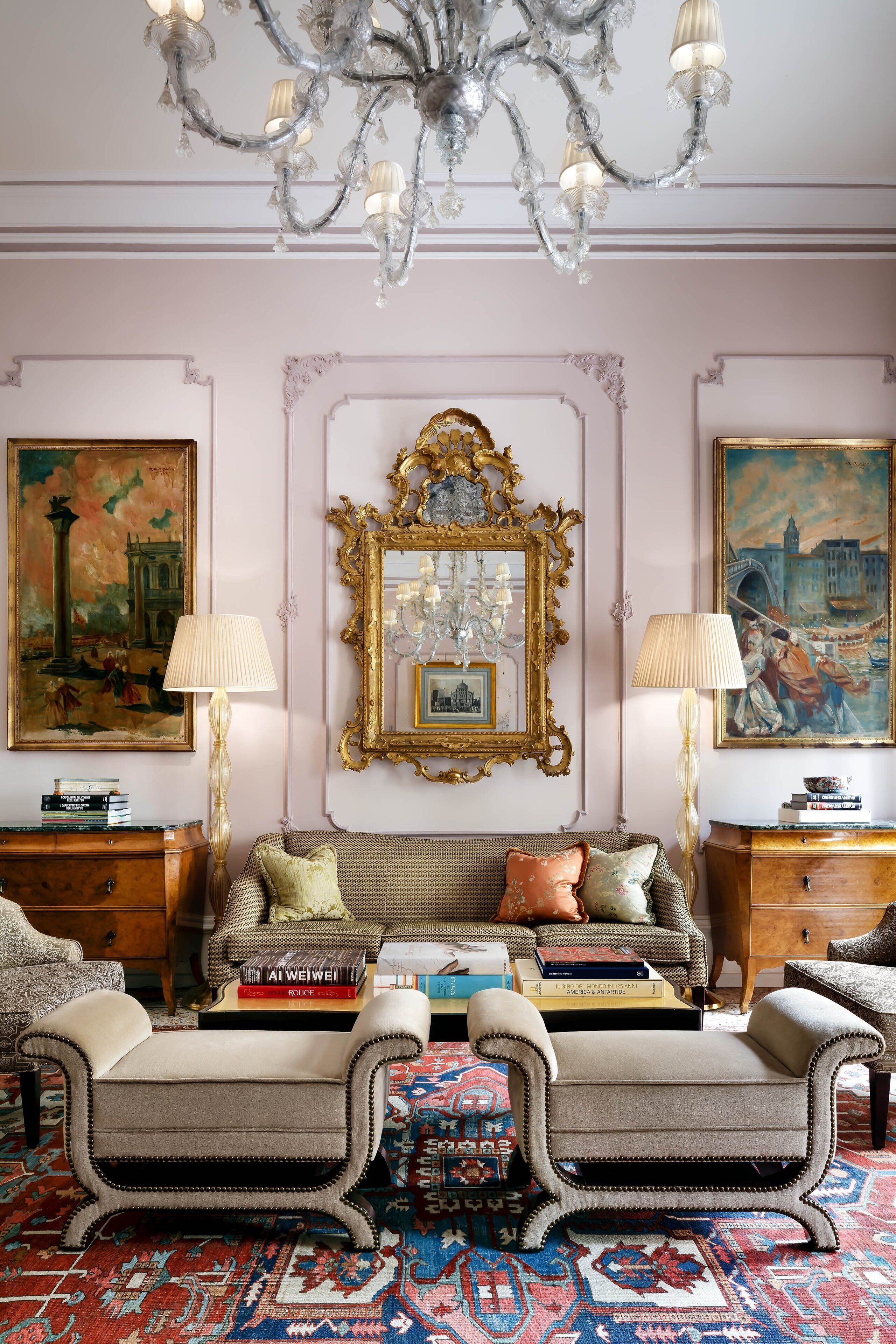 Quarto com design clássico, com um espelho grande e ornamentado, um lustre e um tapete estampado.