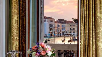 Une pièce dotée d’une grande fenêtre donnant sur un paysage urbain, avec des rideaux décoratifs et une table sur laquelle est posé un vase rempli de fleurs.