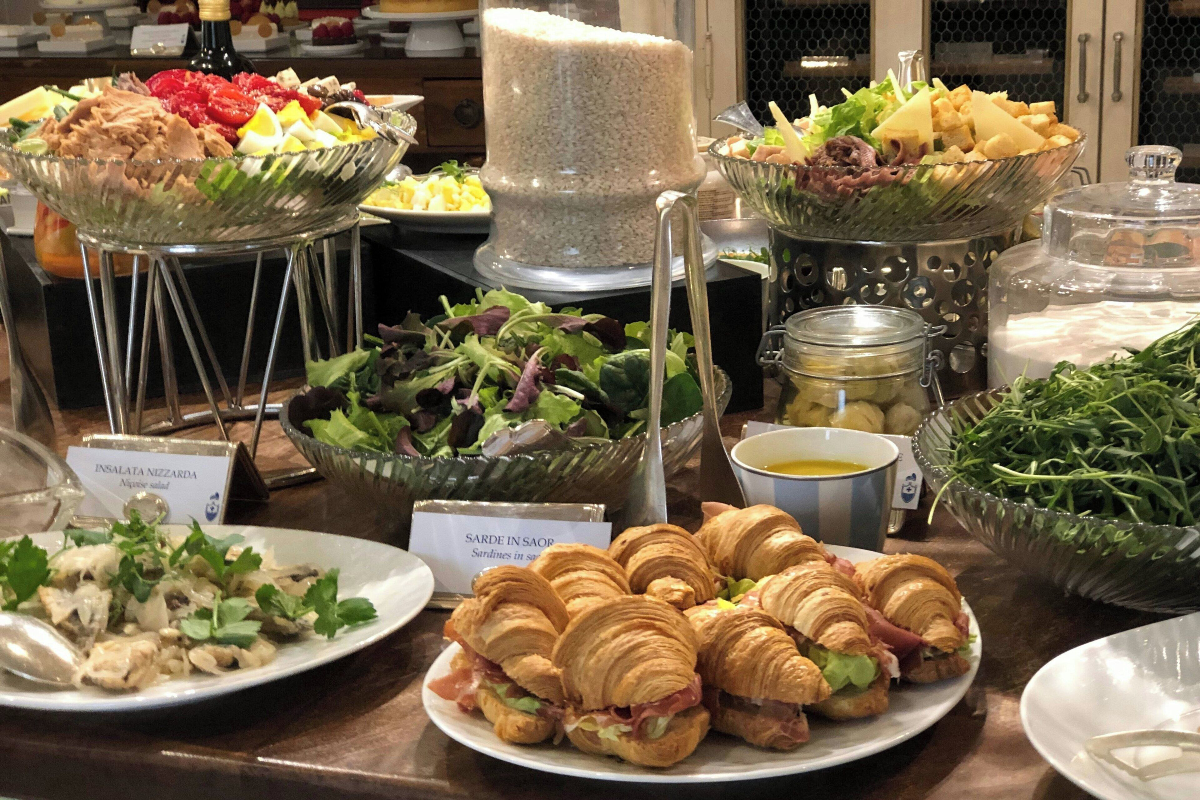 A buffet with various food items including salads, sandwiches, and a large container of rice.