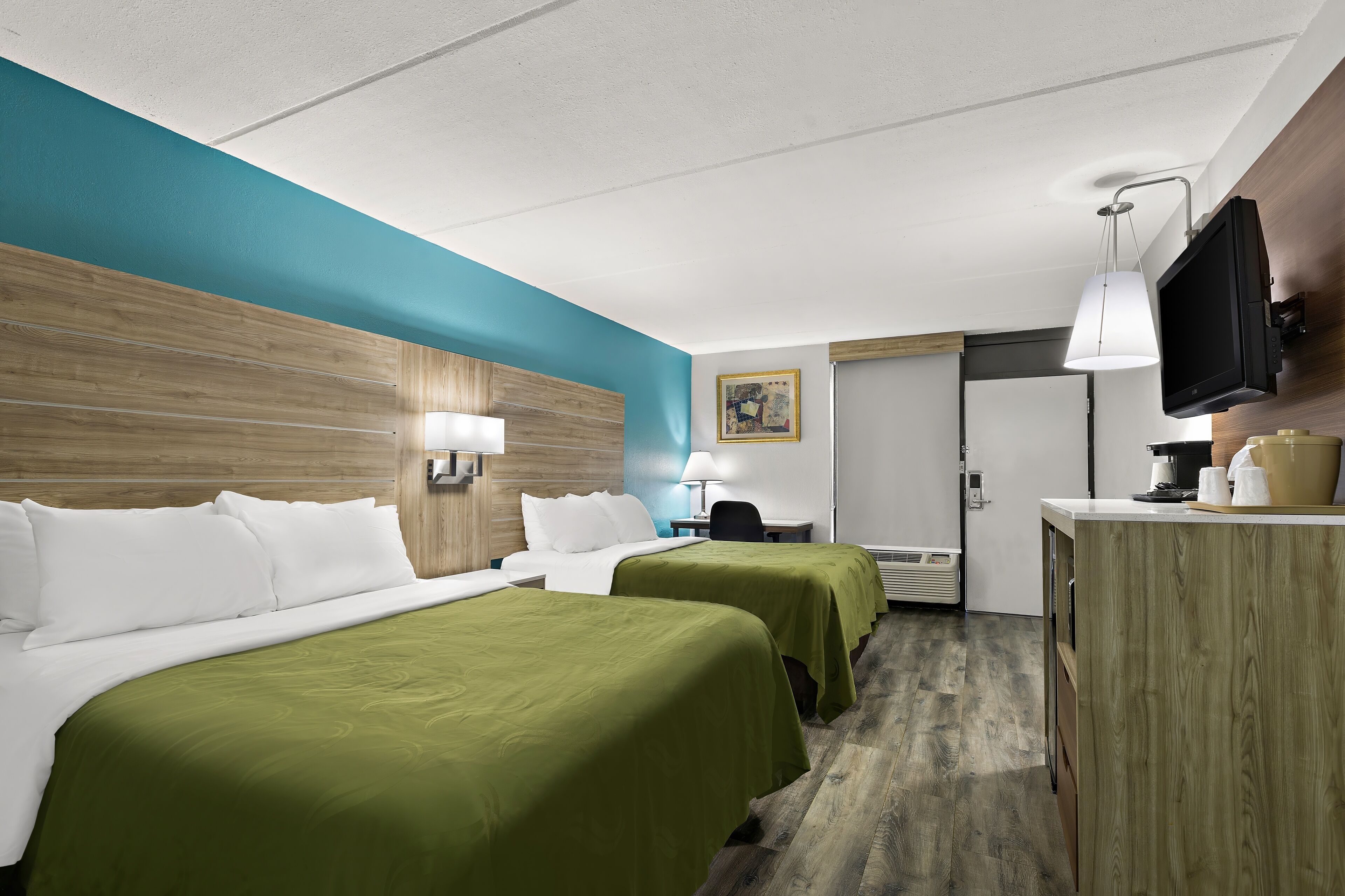 A hotel room with two beds, a desk, a TV, and a painting on the wall.