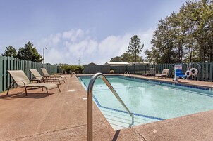 A swimming pool with a metal ladder, lounge chairs, and a lifeguard sign.