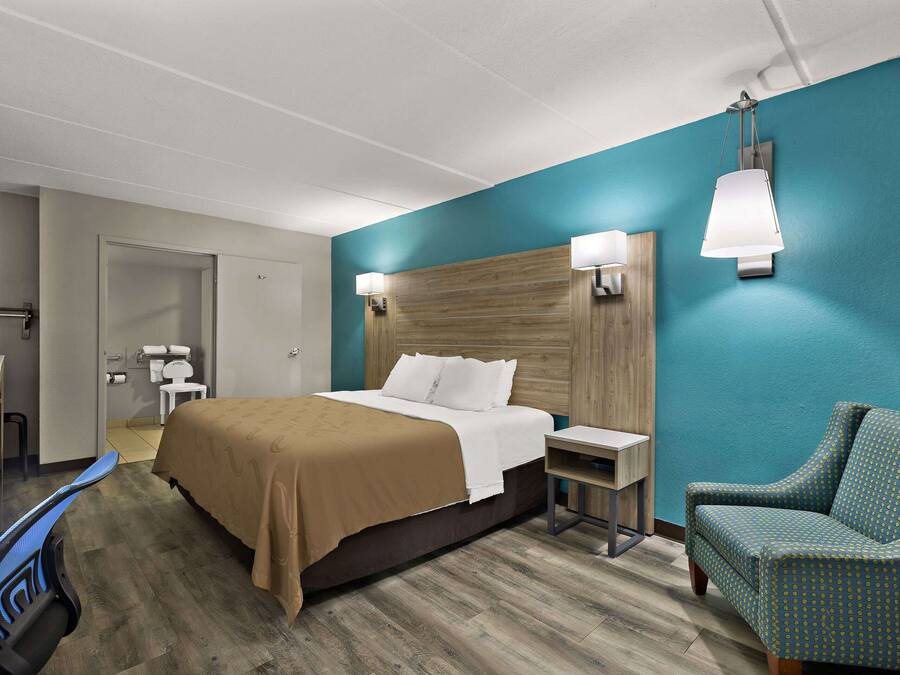 A hotel room with a bed, a chair, a desk, and a bathroom.