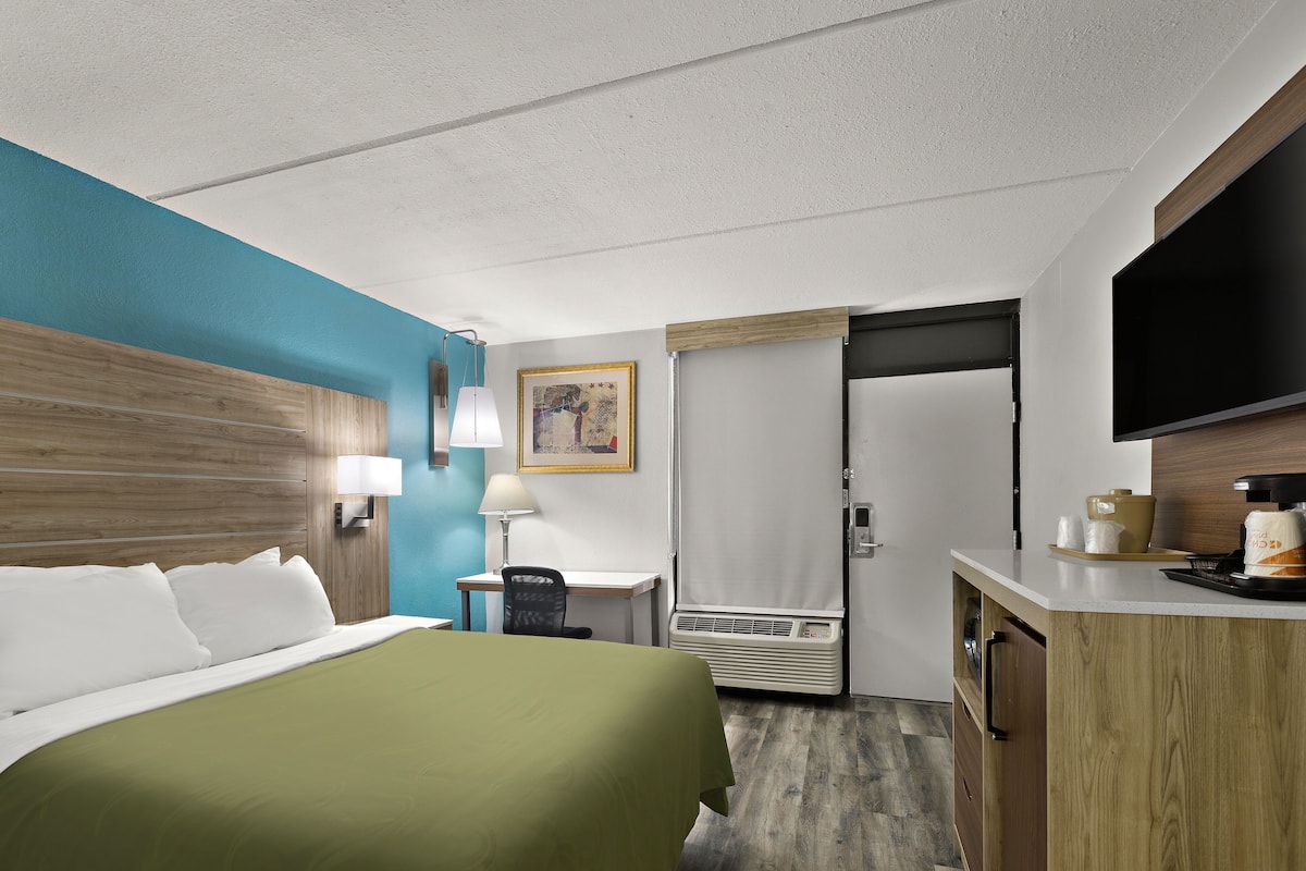 A hotel room with a bed, desk, chair, air conditioning unit, and a television.