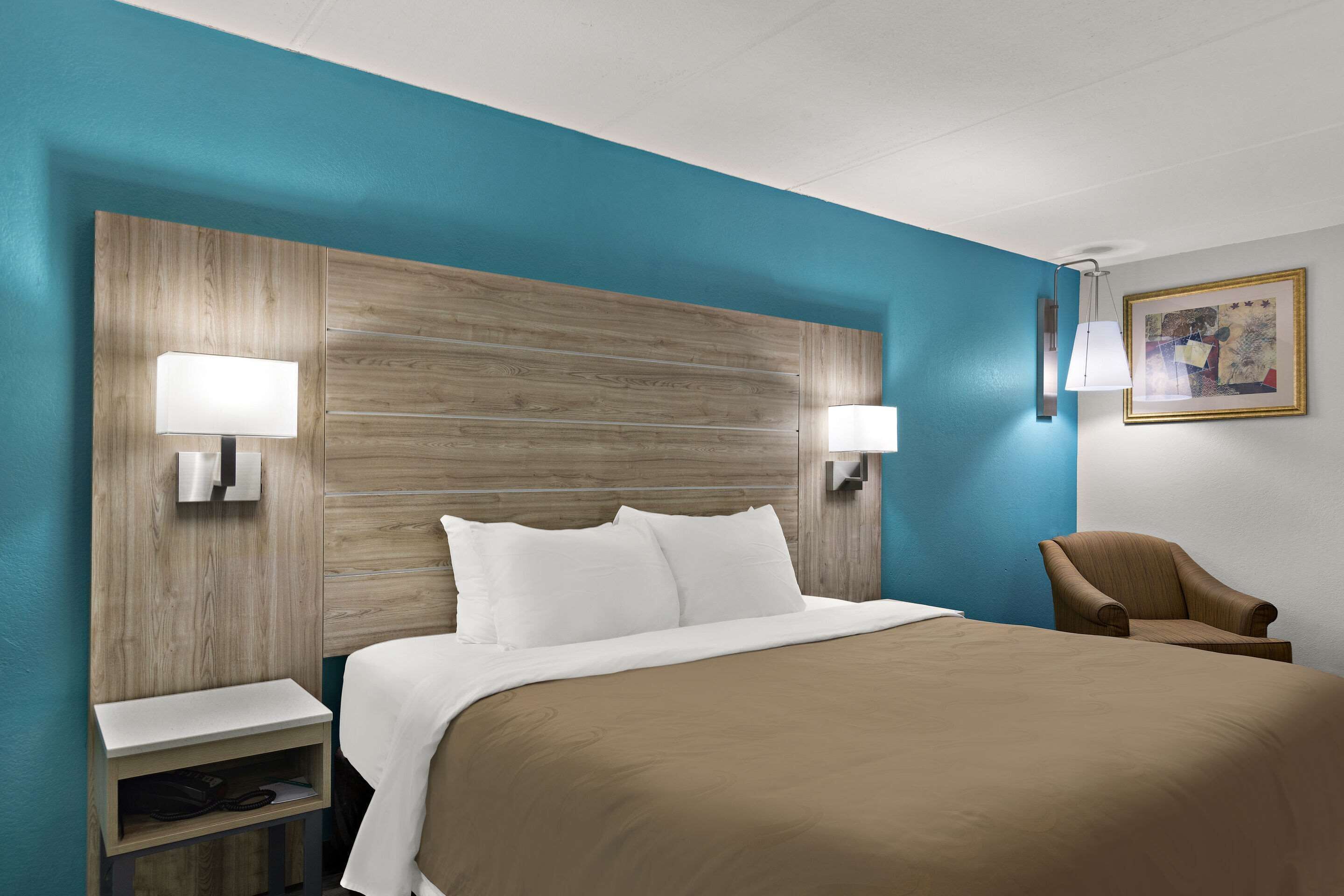 A hotel room with a large bed, two bedside tables, a chair, and a wall-mounted lamp.