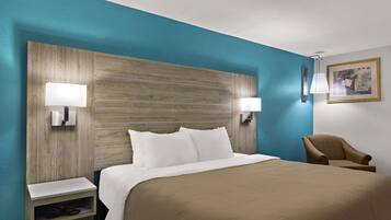A hotel room with a large bed, two bedside tables, a chair, and a wall-mounted lamp.