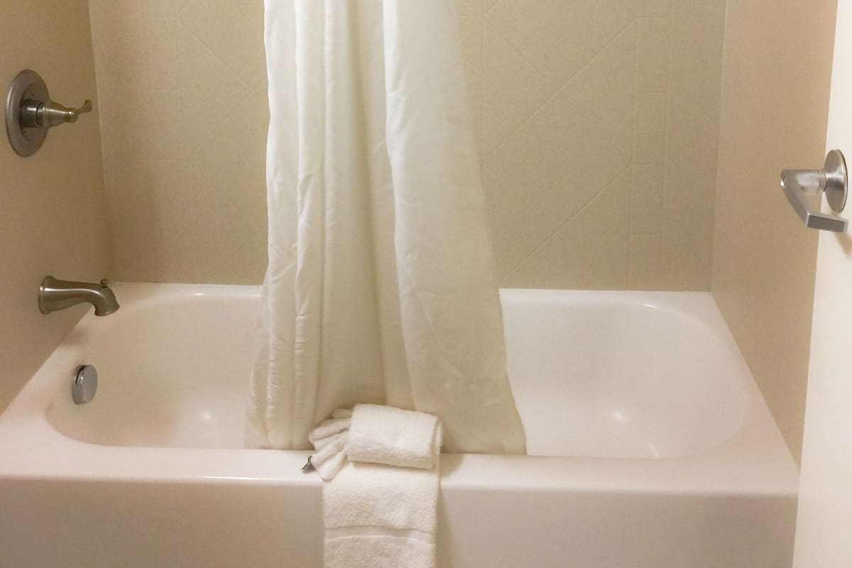 A bathroom with a bathtub, shower, and a white curtain.