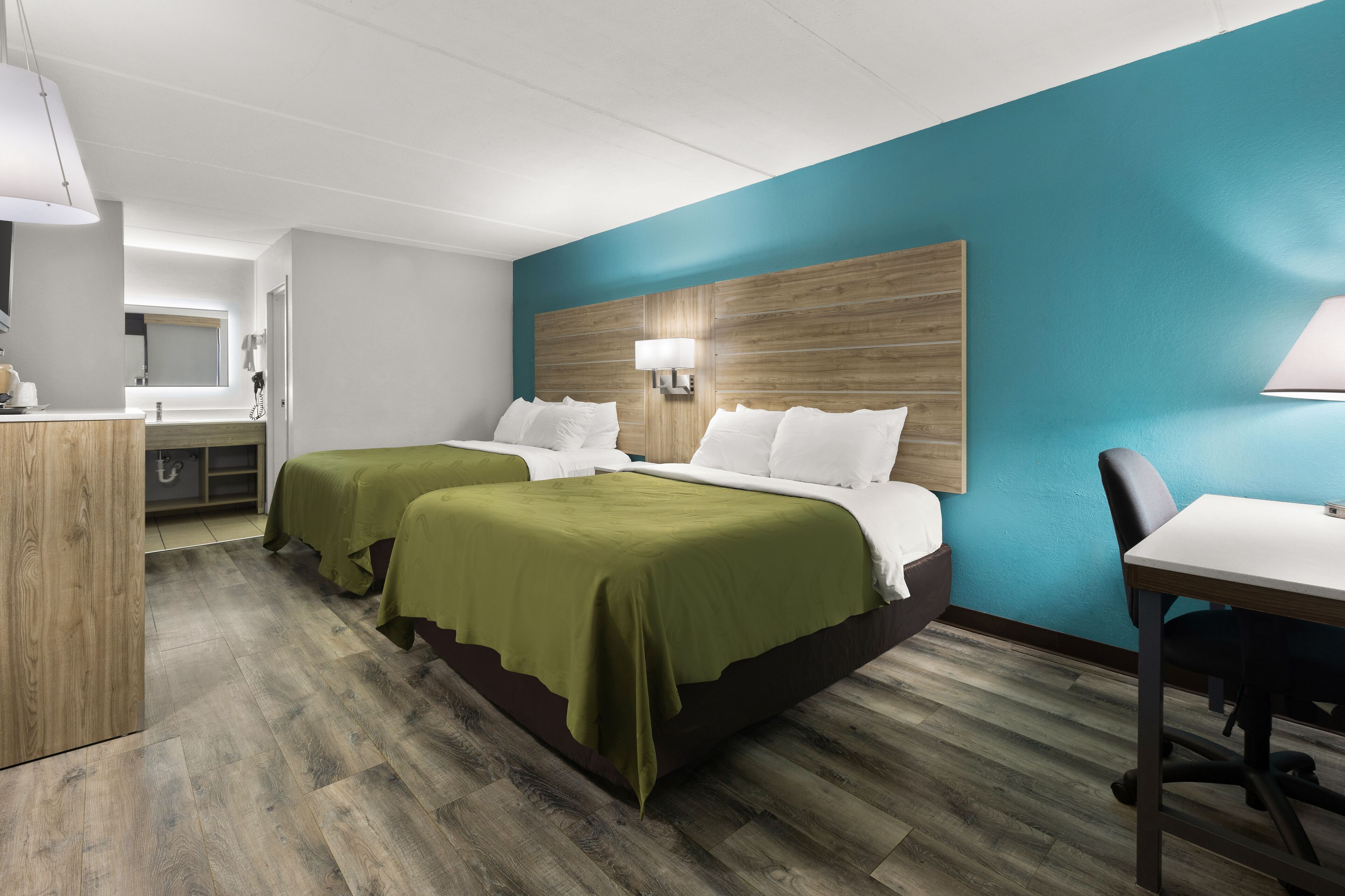 Een hotelkamer met twee bedden, een bureau, een stoel, een spiegel en een houten hoofdeinde.