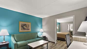 Una habitación de hotel con pared verde azulado, sofá verde, mesa blanca, cama con edredón color beige y un espejo.