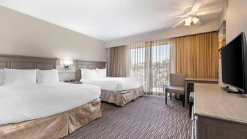 A hotel room with two beds, a desk, a chair, a television, and a ceiling fan.