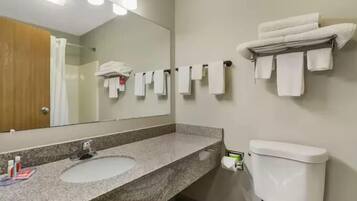 Une salle de bain avec un lavabo doté d’un plan de travail en granit, un miroir, des toilettes et plusieurs serviettes blanches suspendues à un porte-serviettes.