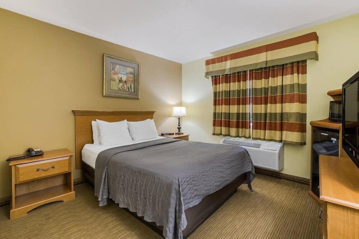 A hotel room with a bed, bedside table, lamp, air conditioning unit, and a television.