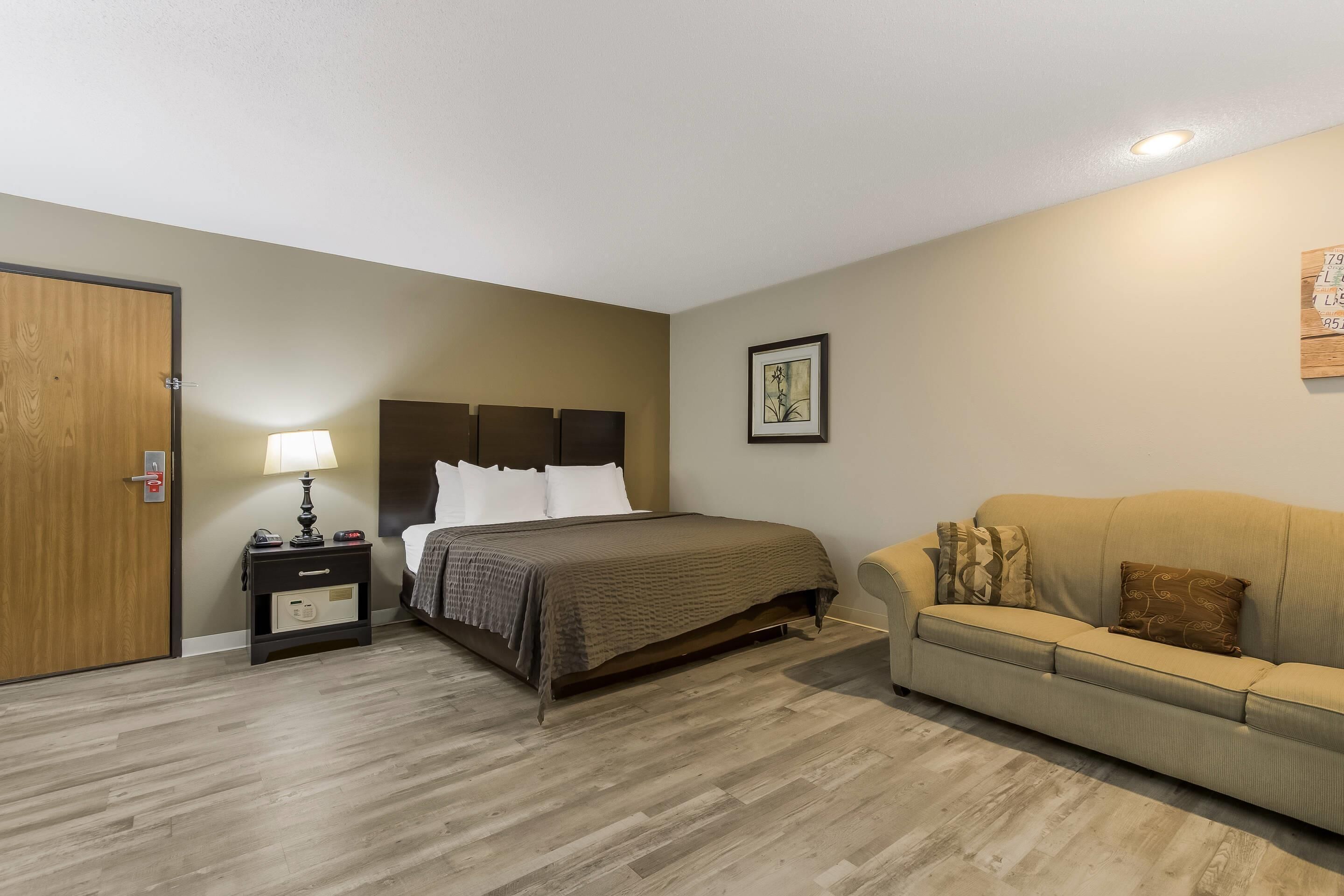 Un dormitorio con cama, mesita de noche, lámpara y sofá.