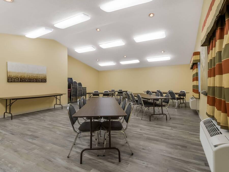 Een vergaderzaal met meerdere tafels en stoelen, plafondlampen en een grote airconditioning.
