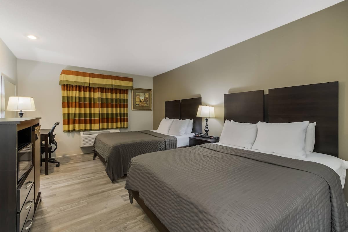 A hotel room with two beds, a desk with a lamp, a chair, and a window with curtains.