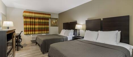 Habitación de hotel con dos camas, un escritorio con lámpara, una silla y una ventana con cortinas.