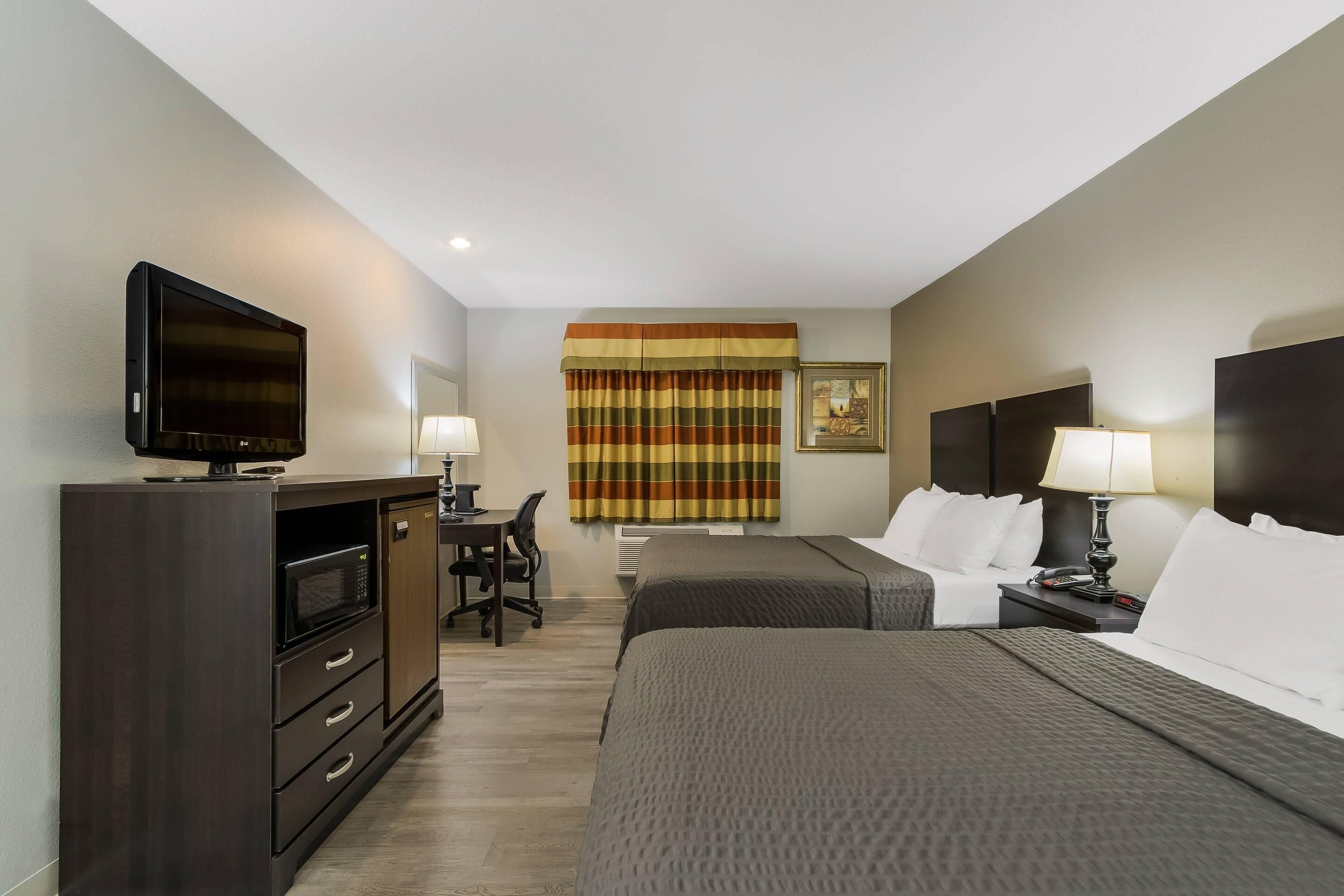 Una habitación de hotel con una cama, un escritorio con una silla, un televisor, una lámpara y una ventana con cortinas.
