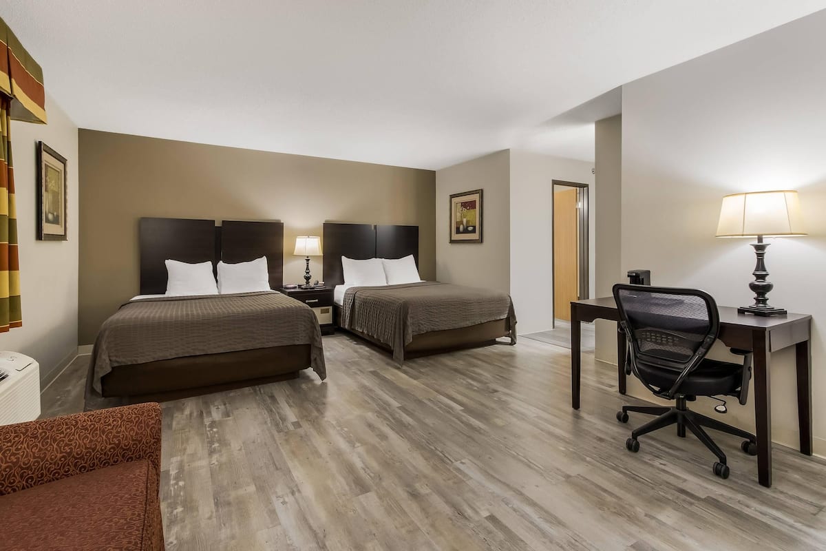 A hotel room with two beds, a desk, a chair, and a lamp.