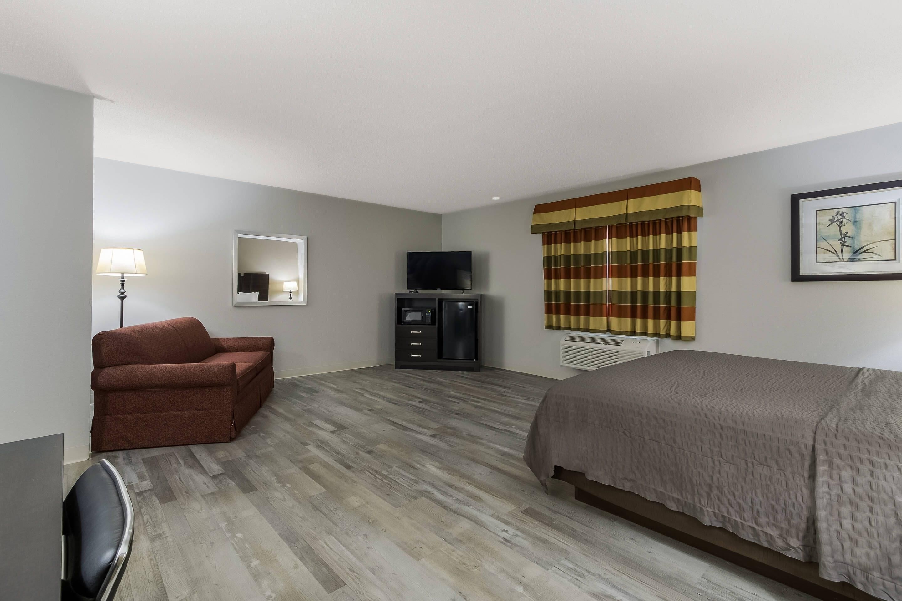 Una habitación de hotel con cama, sofá, televisión, escritorio y espejo.