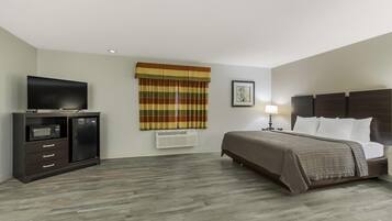 A hotel room with a bed, a TV, a dresser, a window with curtains, and a wall-mounted air conditioner.