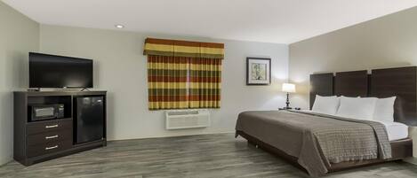 Habitación de hotel con cama, televisión, cómoda, ventana con cortinas y aire acondicionado de pared.