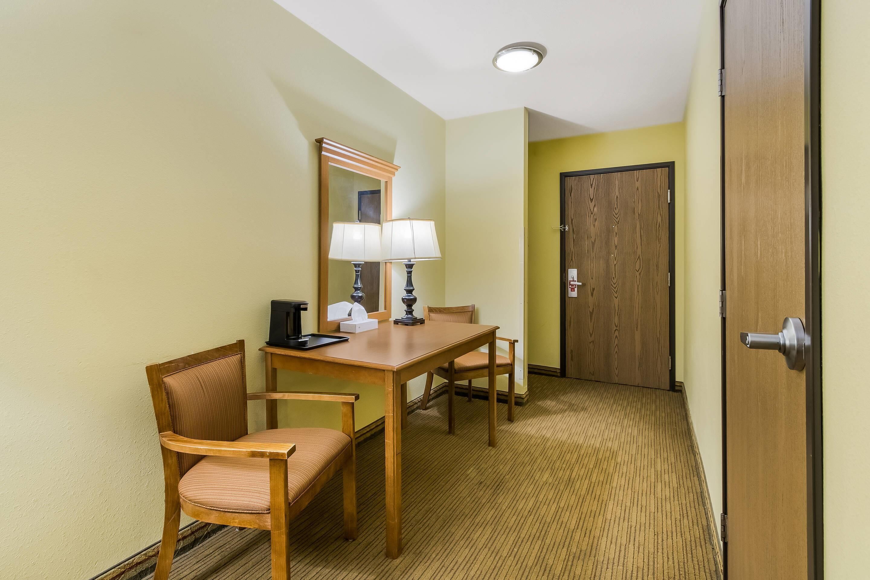 Une chambre d’hôtel avec une table à manger en bois, deux chaises, un miroir, une lampe et une porte.