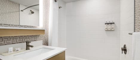 A modern bathroom with a white sink, vanity, and bathtub. There is a showerhead and a towel rack visible.