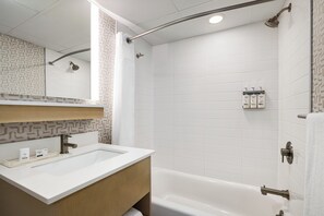 A modern bathroom with a white sink, vanity, and bathtub. There is a showerhead and a towel rack visible.