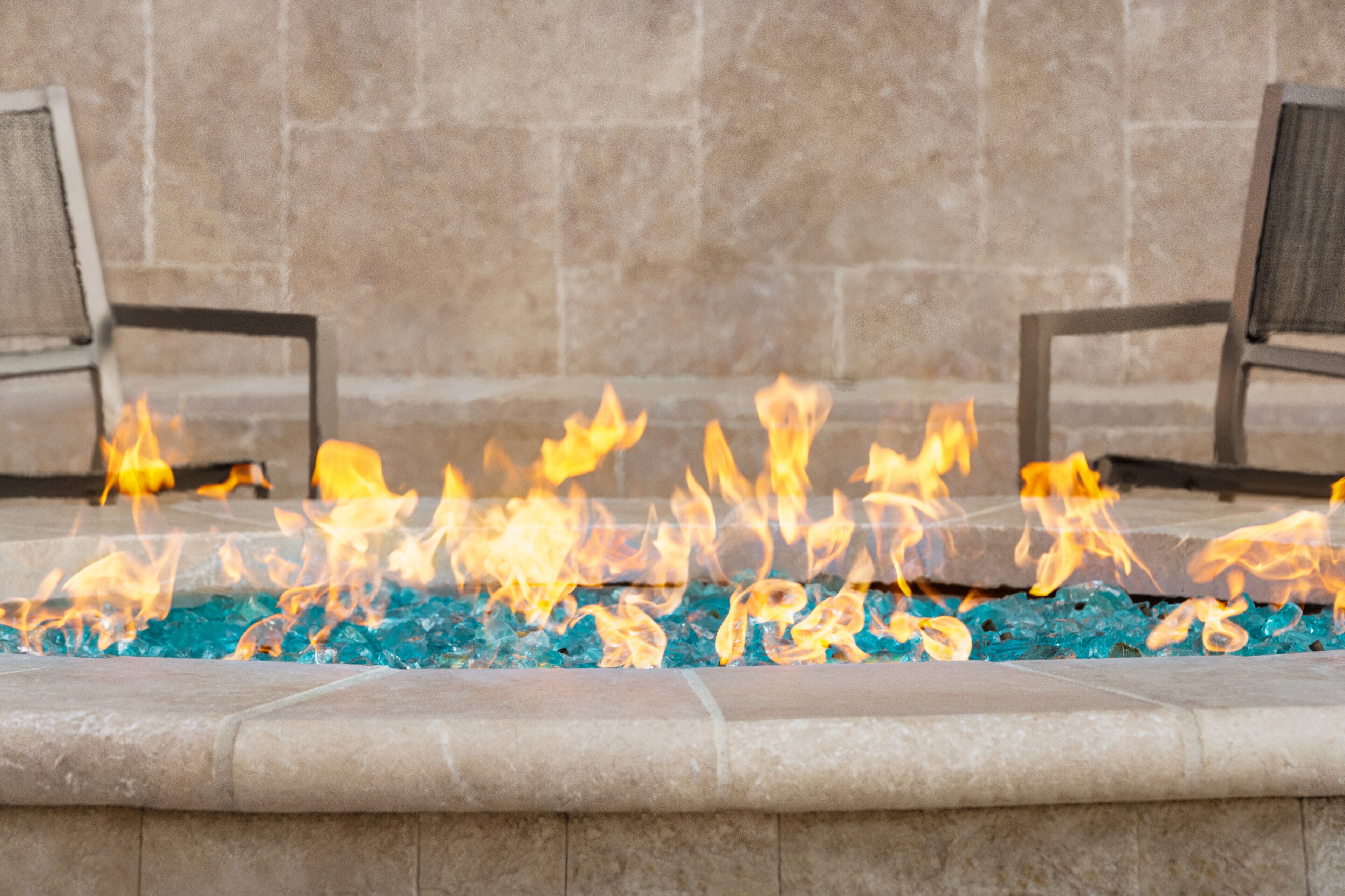 A fire feature with a stone surround and two chairs facing it.