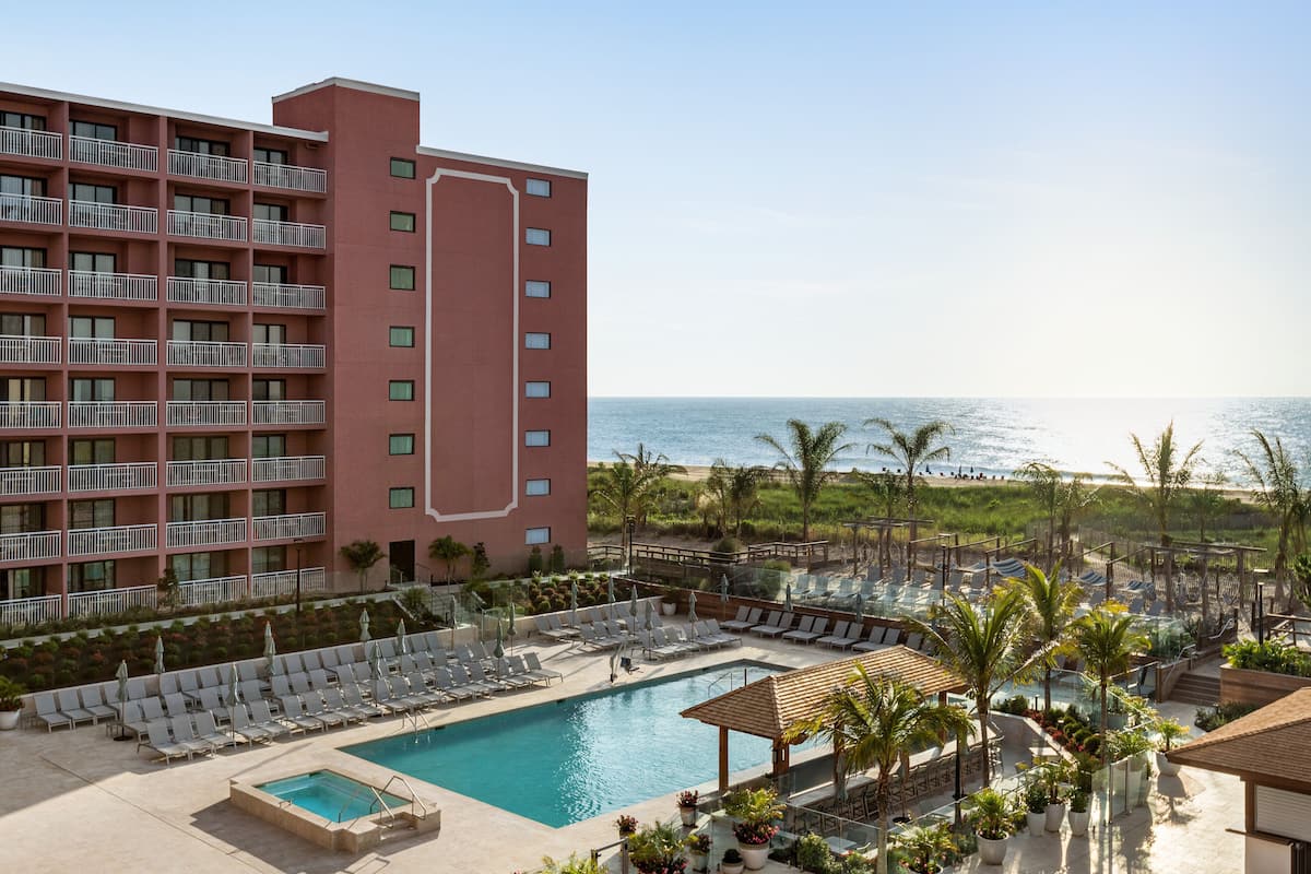 A hotel with a pool, lounge chairs, and a view of the ocean.
