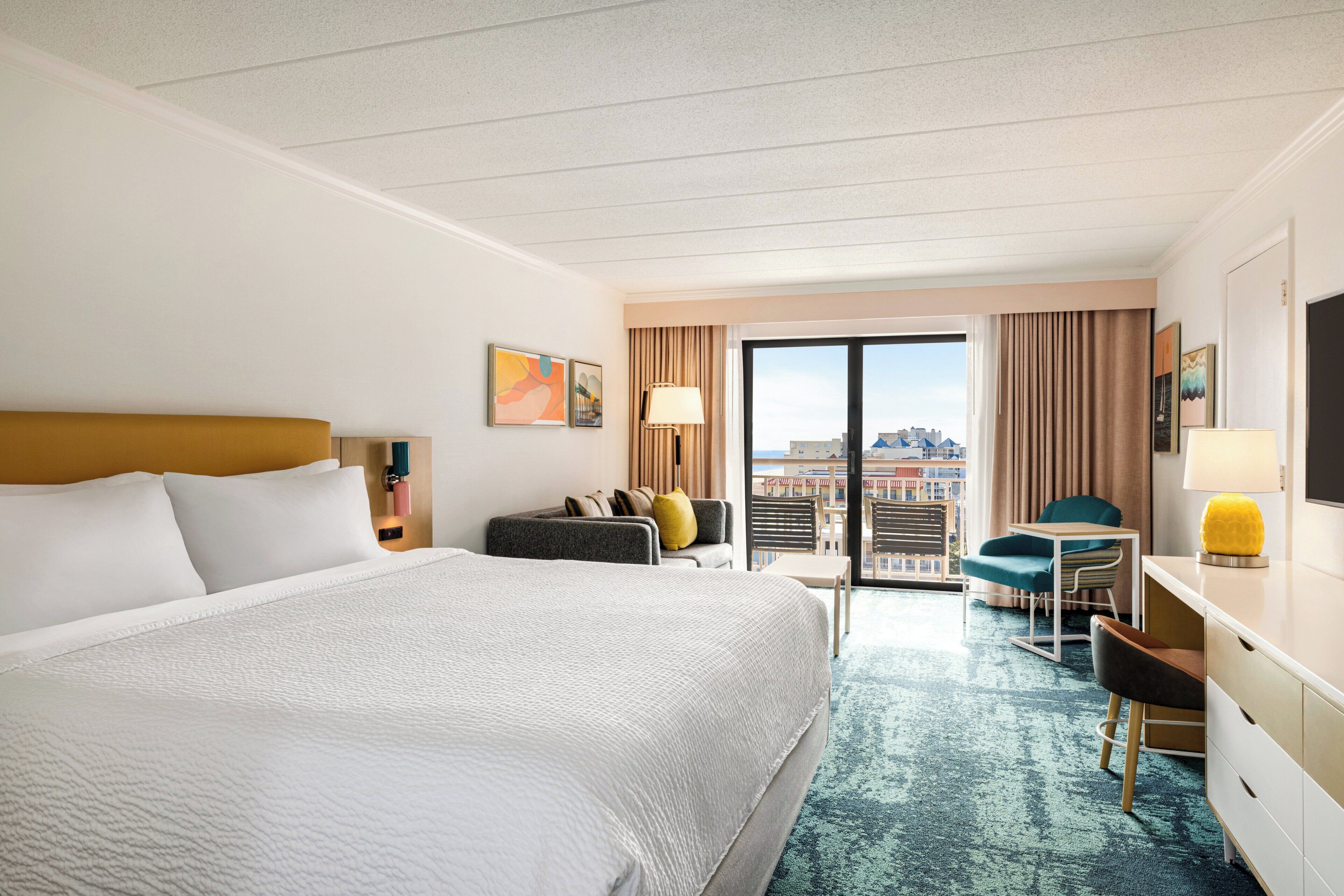A hotel room with a large bed, a desk, a chair, and a view of the city through the window.