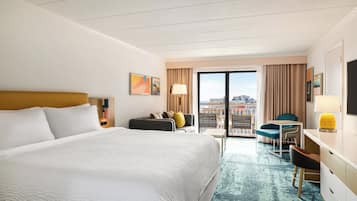 A hotel room with a large bed, a desk, a chair, and a view of the city through the window.