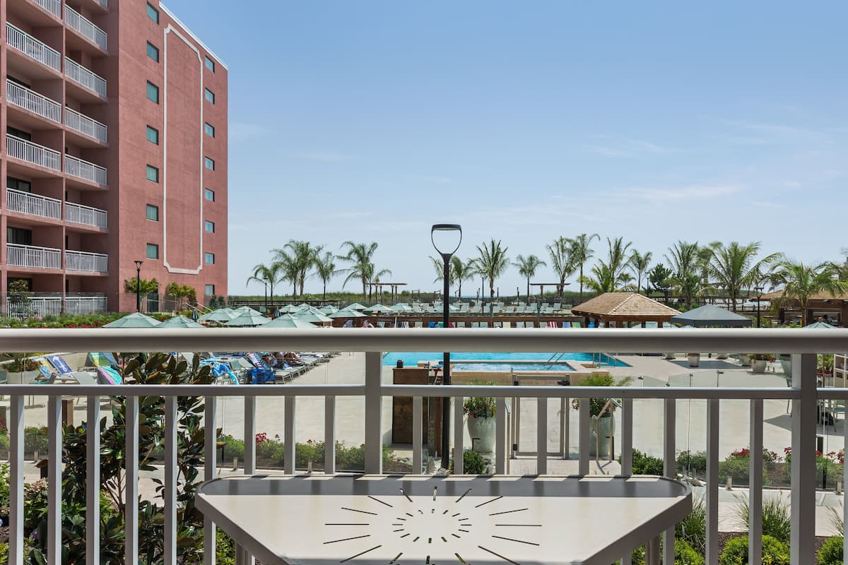 A hotel balcony with a pool, palm trees, and a building with balconies.