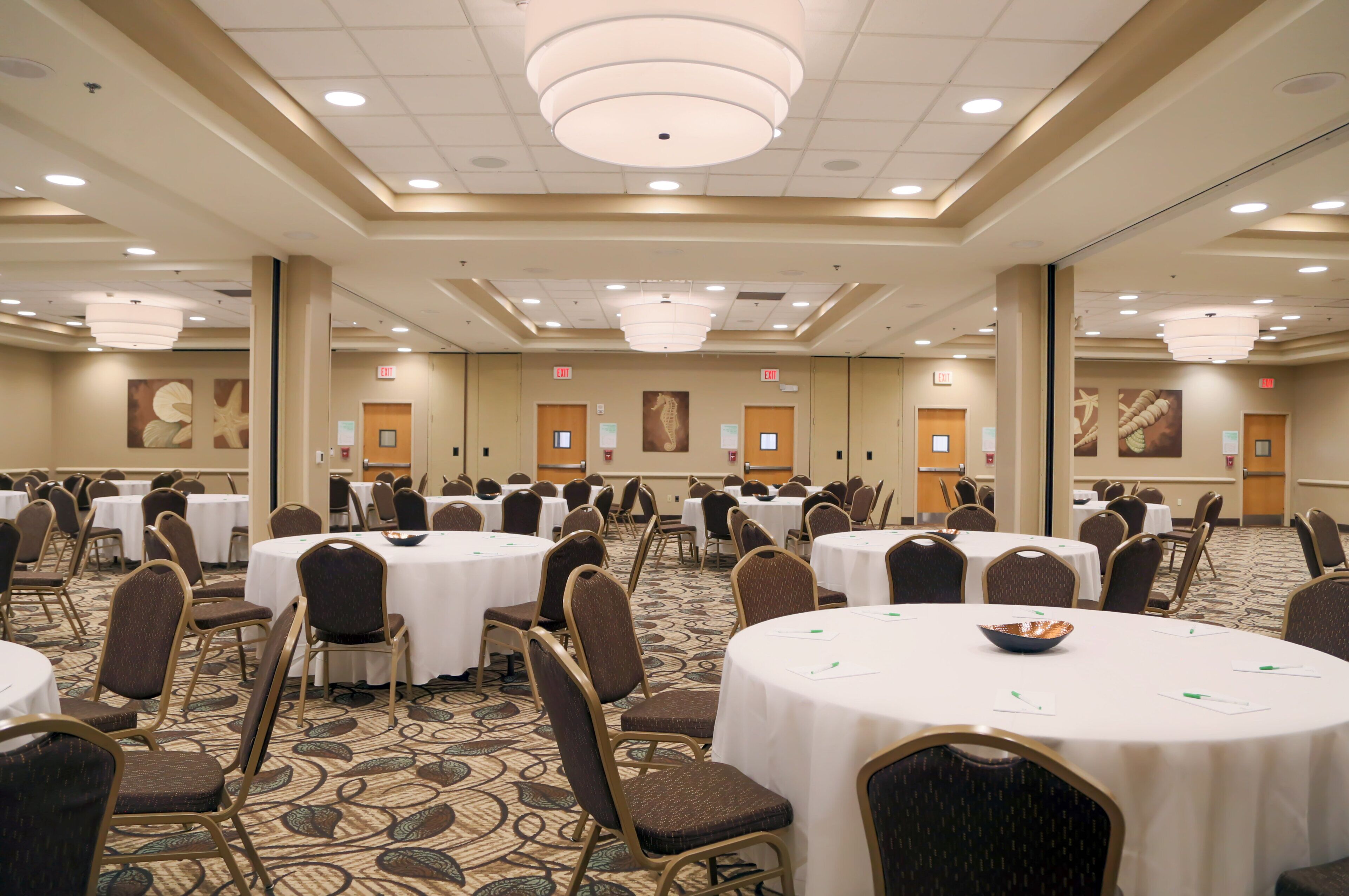 A large conference room with multiple round tables and chairs, equipped with white tablecloths and name cards.