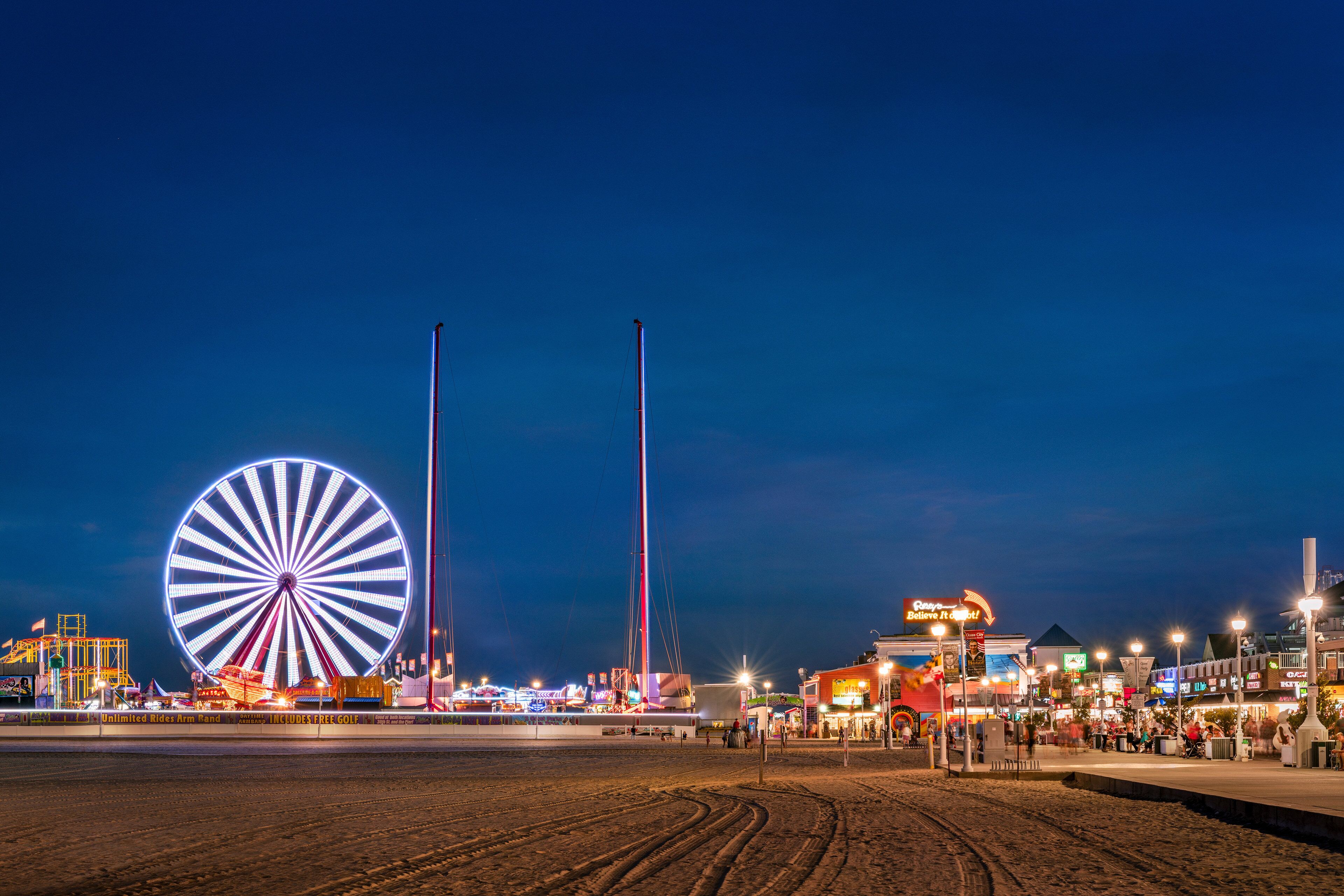 Una noria y estructuras altas en un parque de atracciones frente al mar, de noche.