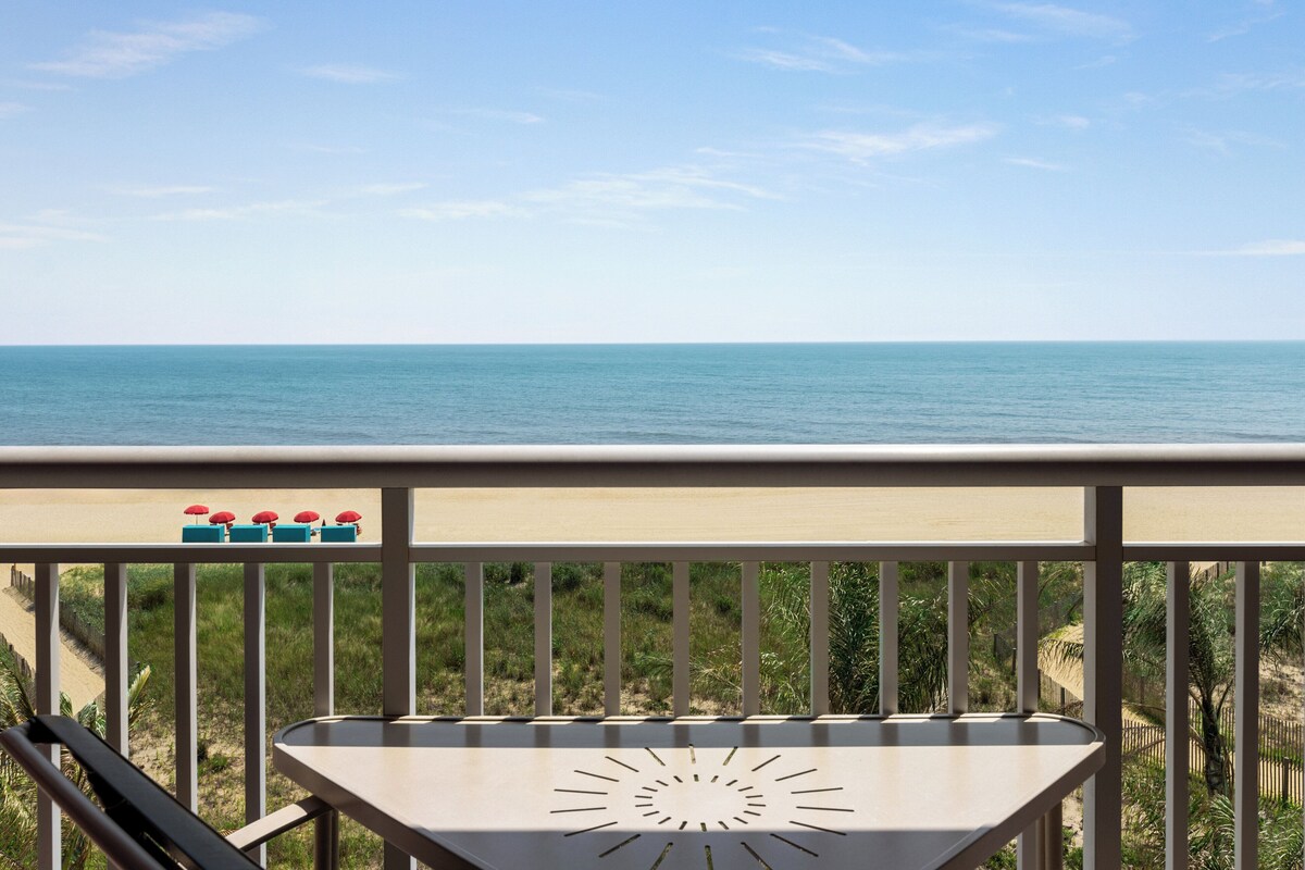 A balcony with a view of the ocean, a table, and a row of umbrellas.