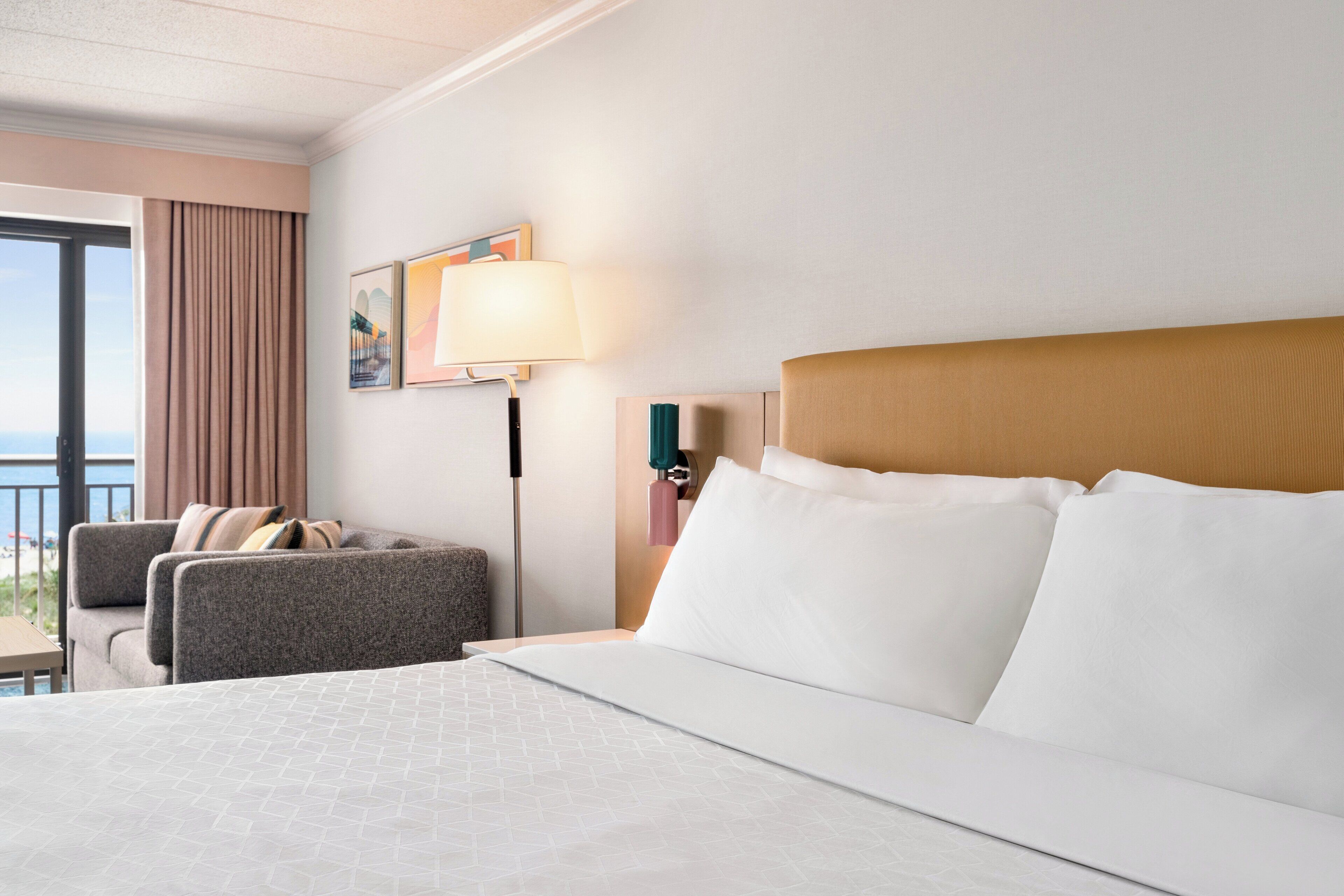 Una camera d'albergo con un letto, un comodino, una lampada, una sedia e vista sull'esterno.