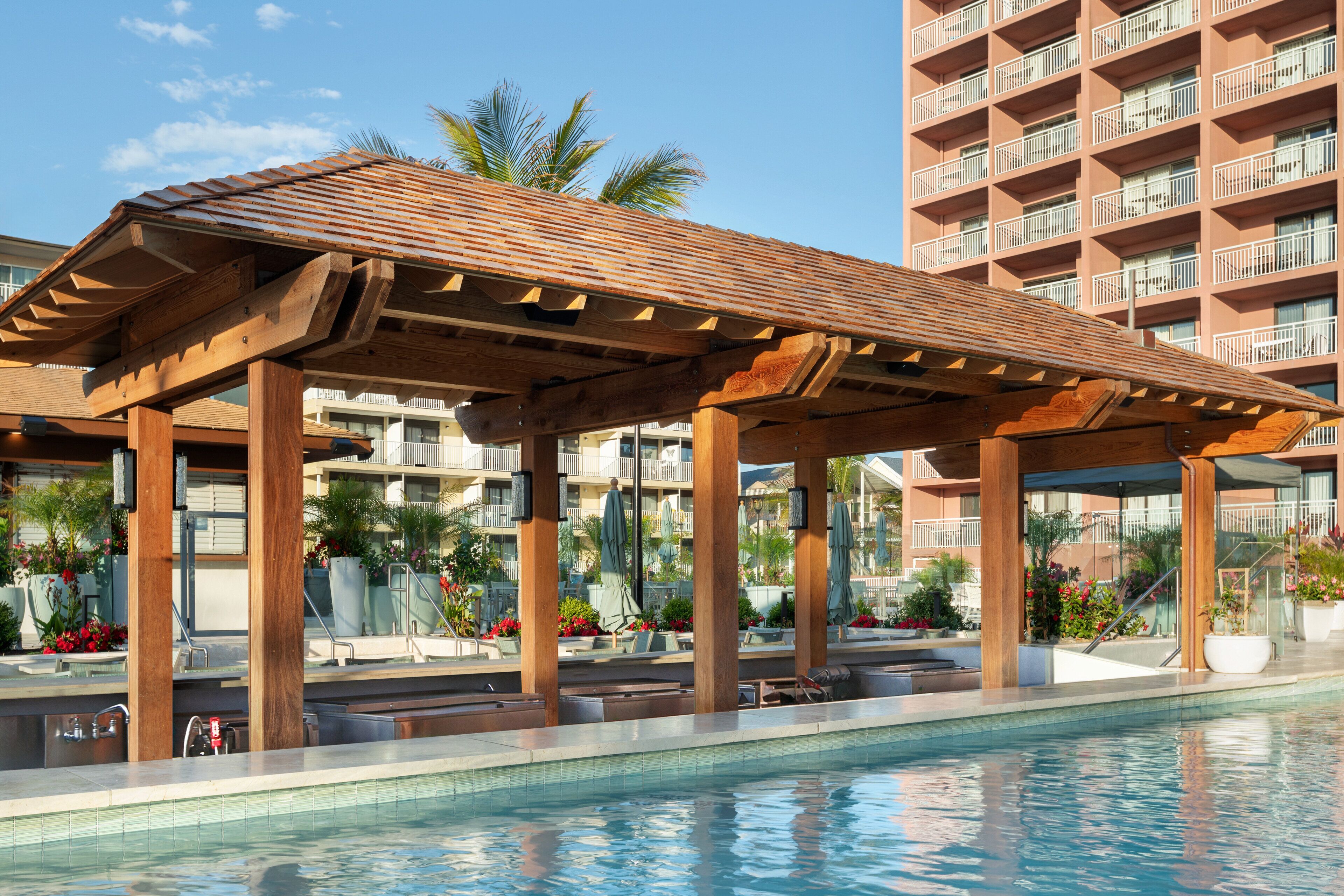 Un espace piscine agrémenté de pergolas en bois, de chaises longues et offrant une vue sur un immeuble à plusieurs étages doté de balcons.