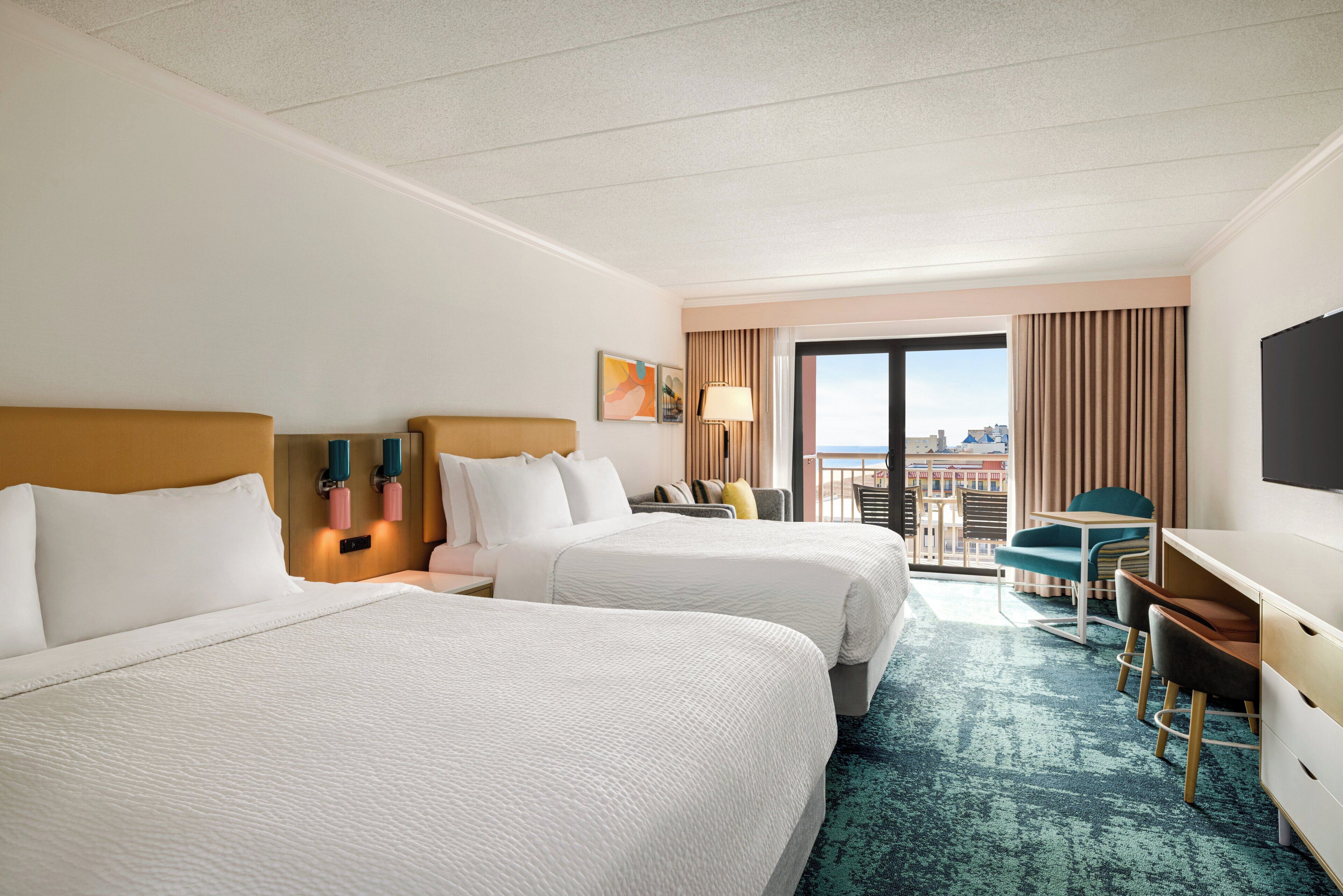 A hotel room with two beds, a desk, a chair, and a large window with a city view.