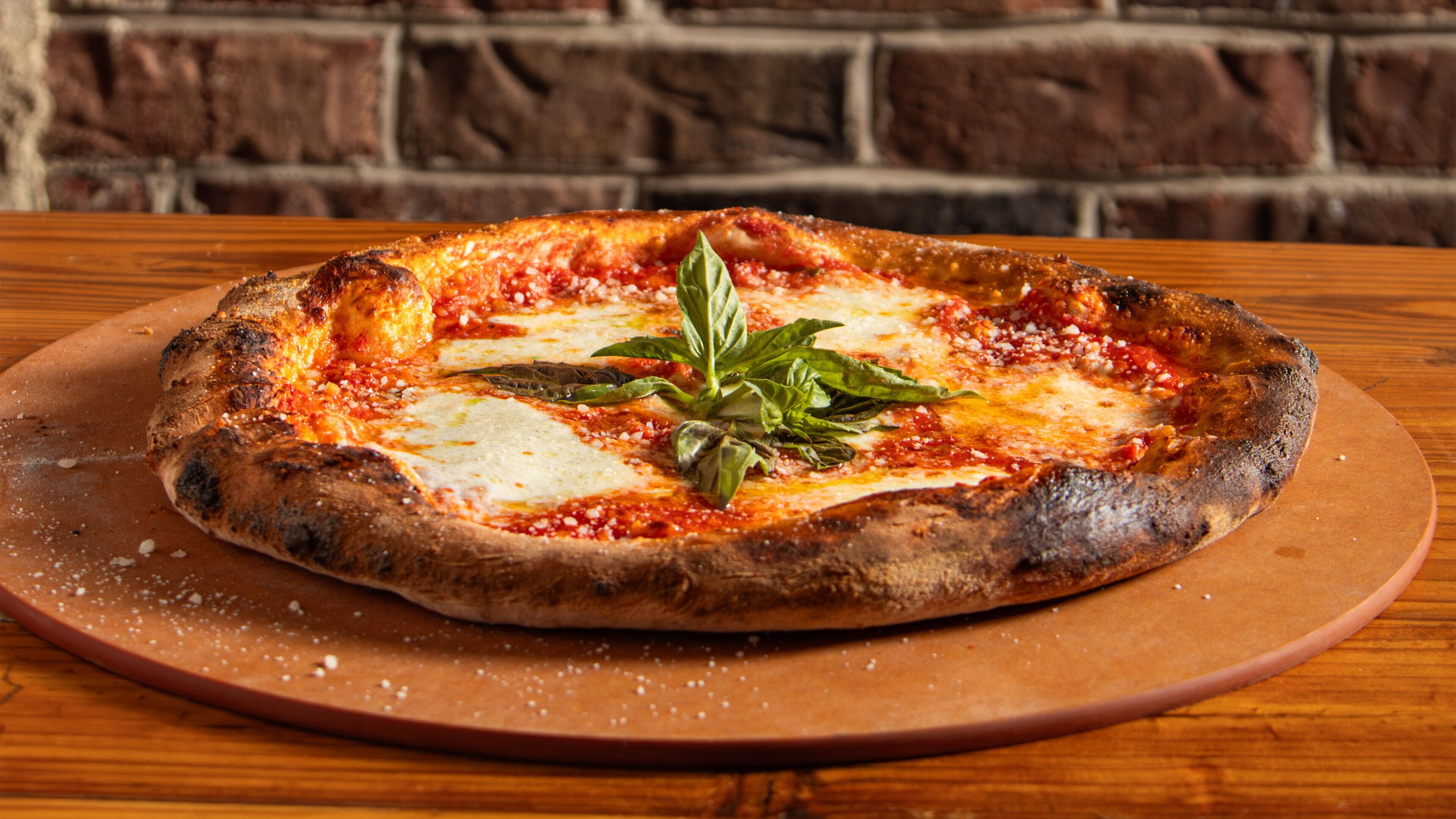 A pizza on a wooden table with a brick wall background.