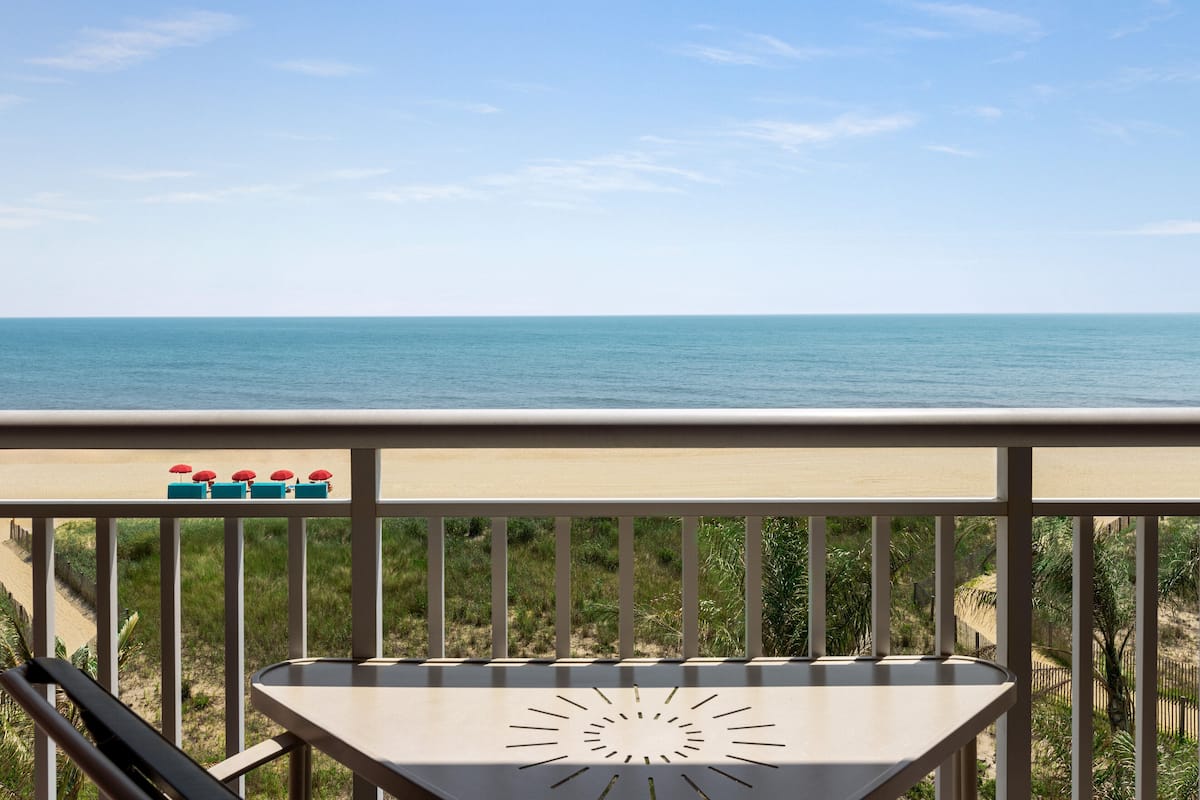 A balcony with a view of the ocean, a table, and a row of umbrellas.
